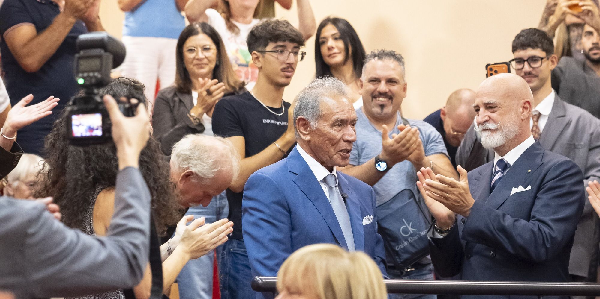 La sala consiliare di Rivoli in piedi applaude Wes Studi e Nicola Paparusso, fra telefoni alzati e una macchina fotografica con il flash